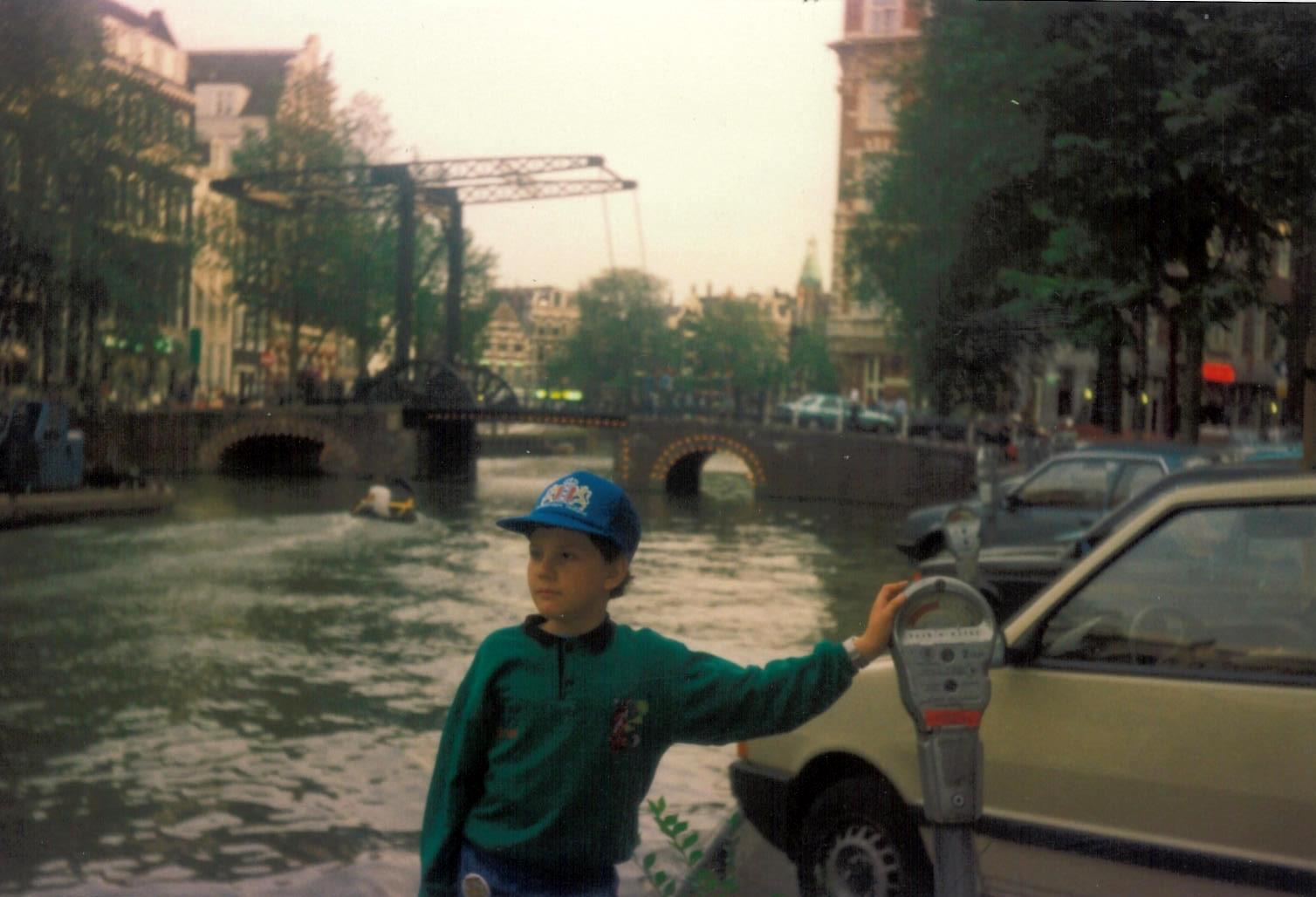 Mihai as a 9-year-old by an Amsterdam canal in 1990, wearing a green sweater and blue cap.