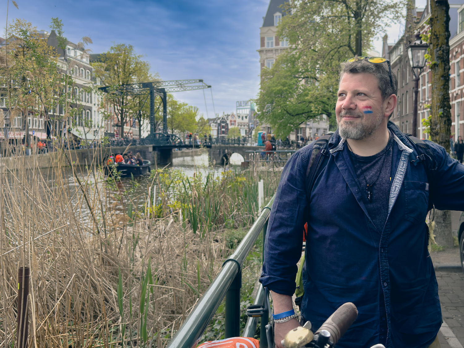 Mihai by the same Amsterdam drawbridge in 2026, with a Romanian flag painted on his cheek.